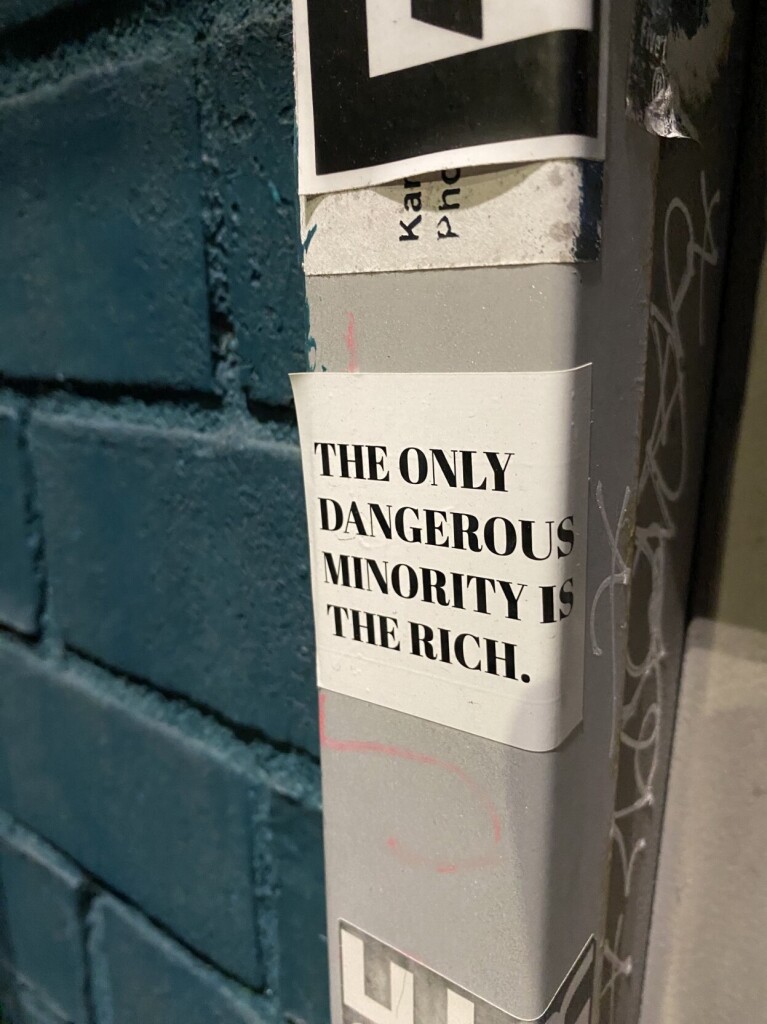 Sticker on a pole that says The only dangerous minority is the rich"