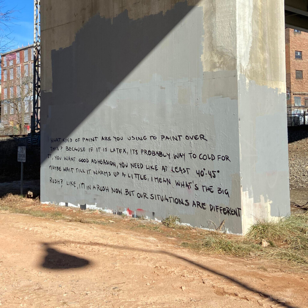 A concrete pillar supporting a bridge with bare soil foreground and buildings out-of-focus in the background.  Old graffiti on the pillar has been covered with dull gray paint, and new graffiti tops it reading,  "What kind of paint are you using to paint over this?  Because if it is latex, its probably way too cold for it, you want good adhesion, you need like at least 40'-45'.  Maybe wait till it warms up a little.  I mean what's the big rush?  Like, I'm in a rush now, but our situations are different."  