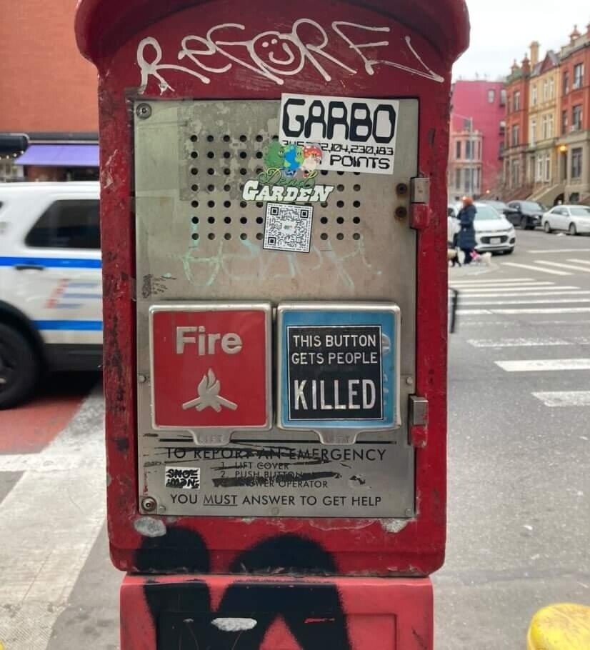 Sticker on a NYPD emergency button on the sidewalk that says "This button gets people killed"