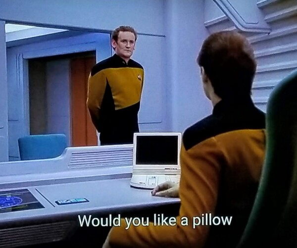 TNG scene. We're in Data's quarters, looking from behind him sitting at his desk with future space laptop type device in the surface. He's looking up at Chief O'Brien, who is looking back at him. Closed caption reads, "Would you like a pillow"